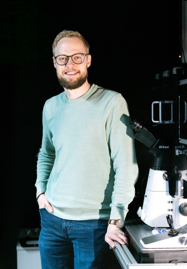 First author Benjamin Springstein standing next to a microscope.